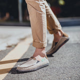 Black woven loafers displayed on a grey road surface, showcasing their breathable and lightweight design with slip-on convenience.