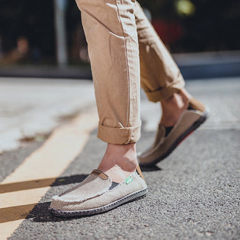 Black woven loafers displayed on a grey road surface, showcasing their breathable and lightweight design with slip-on convenience.