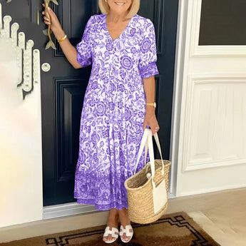 Purple and blue bohemian midi dress with a floral pattern, featuring sleeves and pockets; modeled by a smiling woman, showcasing a relaxed fit around the waist; the dress is suitable for summer occasions.