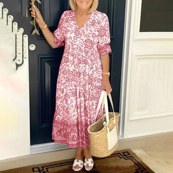 Blue floral bohemian midi dress with pockets in rose color, featuring short sleeves and a cinched waist, modeled by a smiling woman standing with a handbag; perfect for a summer outfit.
