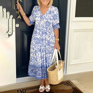 
A smiling woman wearing a blue floral bohemian midi dress with sleeves and pockets, suitable for summer. The dress is a one-piece garment in a 3XL size, showcasing a relaxed fit with a defined waist.