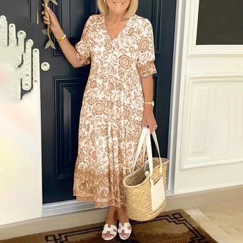 Blue floral bohemian midi dress with pockets, featuring khaki color, worn by a smiling woman. The dress is a one-piece garment with sleeves, suitable for summer wear, and the woman is accessorized with a bag.
