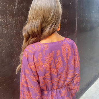 Woman wearing a blue floral midi dress with a V-neck and long sleeves, styled for fall fashion with layered hair and bangs.