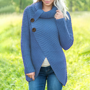 
A woman wearing a blue oversized chunky knit sweater with buttons, styled as part of a fall fashion look. The sweater features a cozy fit with long sleeves and a collar, paired with jeans. The setting suggests a casual, autumnal atmosphere.