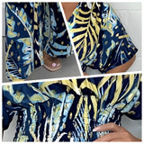 Blue tropical leaf print maxi dress with an elegant V-neck design, featuring short sleeves and flowing fabric in various shades of blue, perfect for a summer setting.