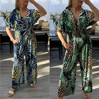 Elegant V-neck maxi dress with blue tropical leaf print, featuring short sleeves and a cinched waist. The model is standing, showcasing the dress's flattering fit and summer-ready style.