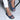 A woman wearing a white dress and blush pink low heel ballet flats, showing her legs from knee to feet, standing on a grey surface.