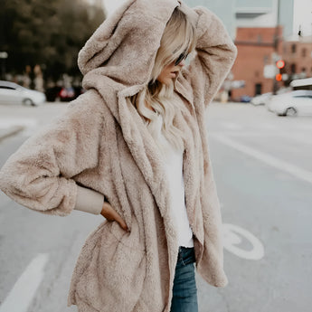 Blush pink women's teddy bear faux fur coat styled with cozy winter wear, featuring a soft, plush texture. The model wears the coat over casual jeans, showcasing a relaxed, oversized fit with long sleeves and an open front design in an apricot color, size 2XL.