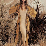 A person wearing a Bohemian beige kimono with a boho-chic tribal pattern, standing in a natural desert setting with grass and plants in the background.