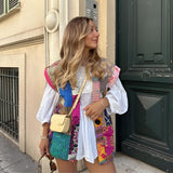 Bohemian embroidered patchwork dress with intricate designs, worn by a woman standing near a window, showcasing unique fashion style with short sleeves and fitted waist, accessorized with sunglasses.