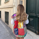 Bohemian embroidered patchwork dress featuring a vibrant mix of purple textiles with intricate designs, showcasing a sleeveless style and a flattering waistline. The model stands in front of a door, highlighting the dress's unique artisan summer fashion appeal.