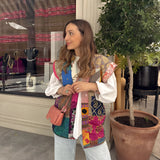 Bohemian embroidered patchwork dress featuring vibrant colors and intricate designs, worn by a smiling woman with styled hair against a backdrop of lush plants. The dress showcases a fashionable collar, sleeves, and a defined waist, emphasizing a casual summer look.