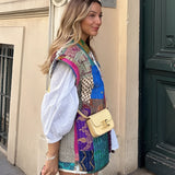 Bohemian Embroidered Patchwork Dress featuring a vibrant mix of textiles, showcasing intricate embroidery and colorful patterns. The dress has a sleeveless design, highlighting the shoulders and neck area, perfect for summer fashion. The model wearing the dress smiles, exuding a joyful and carefree vibe, complemented by her stylish hairstyle.