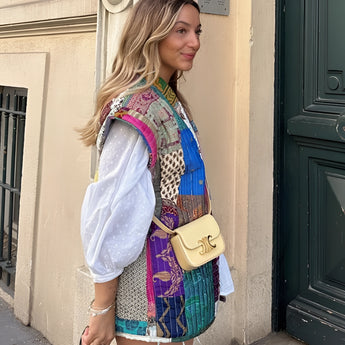 Bohemian Embroidered Patchwork Dress featuring a vibrant mix of textiles, showcasing intricate embroidery and colorful patterns. The dress has a sleeveless design, highlighting the shoulders and neck area, perfect for summer fashion. The model wearing the dress smiles, exuding a joyful and carefree vibe, complemented by her stylish hairstyle.