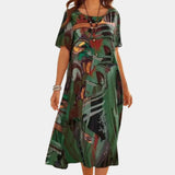 Colorful abstract print bohemian midi dress in green, featuring a loose fit ideal for summer. The dress is knee-length, with short sleeves and a scoop neckline, modeled by a person standing outdoors.