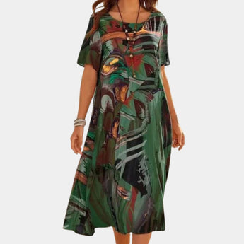 Colorful abstract print bohemian midi dress in green, featuring a loose fit ideal for summer. The dress is knee-length, with short sleeves and a scoop neckline, modeled by a person standing outdoors.