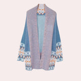 
A light blue oversized Aztec knit sweater for women, featuring a bohemian design with a high neckline and long sleeves, displayed on a clothes hanger. The sweater has a cozy woolen texture, suitable for winter fashion.
