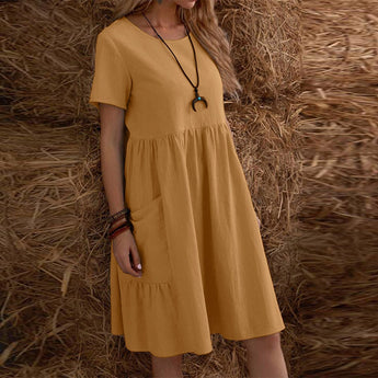 Bohemian tiered midi dress in beige and grey, featuring a scoop neck and short sleeves, designed for plus sizes. The dress is showcased in a natural setting with wooden accents and plants in the background.