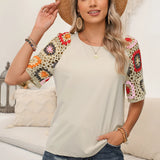 Boho Chic Black Blouse with Floral Crochet Sleeves in Beige, featuring a relaxed fit and detailed crochet sleeves. Model wearing size 2XL, smiling and posing with a casual hat.