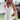 
A woman wearing a boho-chic crochet back sundress in white, size 2XL, accessorized with a wide-brimmed sun hat and sunglasses, standing outdoors under a clear sky. The dress features a sleeveless design, fitted at the waist and flowing to mid-thigh.
