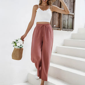 Woman wearing a white lace top and rust palazzo pants with a straw hat and sunglasses, showcasing boho chic resort wear.