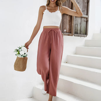 Woman wearing a white lace top and rust palazzo pants with a straw hat and sunglasses, showcasing boho chic resort wear.