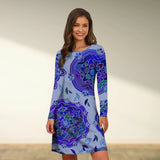 
Woman wearing a blue boho chic tribal print A-line knee-length dress, featuring a round neckline and sleeves, standing amid greenery and smiling.