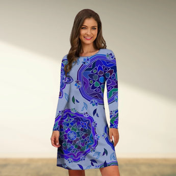 
Woman wearing a blue boho chic tribal print A-line knee-length dress, featuring a round neckline and sleeves, standing amid greenery and smiling.