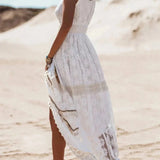 White lace maxi dress in boho chic style worn by a woman on a beach. The dress features a delicate lace pattern and extends to the ankles, ideal for summer beach weddings. The woman appears joyful, with the sky in the background adding to the serene setting.