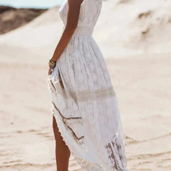 White lace maxi dress in boho chic style worn by a woman on a beach. The dress features a delicate lace pattern and extends to the ankles, ideal for summer beach weddings. The woman appears joyful, with the sky in the background adding to the serene setting.