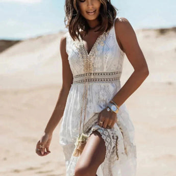Boho chic white lace maxi dress with long sleeves and a fitted waist, worn by a woman with long hair against a clear sky backdrop, ideal for a summer beach wedding.