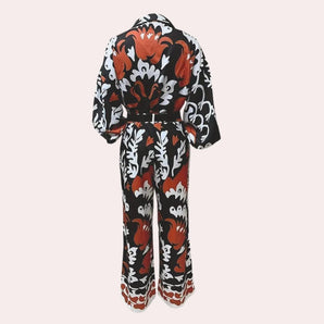 Orange, black, and white floral patterned long sleeve jumpsuit with a belted waist.