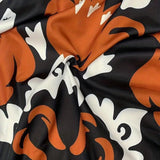 Orange, black, and white long sleeve jumpsuit featuring a bold floral pattern with a belted waist.