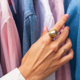 A close-up of a hand wearing a Bold Gold Adjustable Statement Ring with a Large Reflective Gemstone, showcasing the ring's intricate design and shiny gemstone, against a background of a person in a suit and tie.