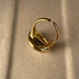 A bold gold adjustable statement ring featuring a large reflective gemstone, showcasing intricate design and luxurious craftsmanship.