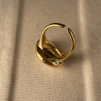 A bold gold adjustable statement ring featuring a large reflective gemstone, showcasing intricate design and luxurious craftsmanship.