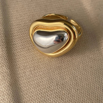 Bold gold adjustable statement ring with large reflective gemstone, close-up view showing intricate details and shimmering surface.