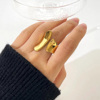 A woman's hand wearing a modern, sculptural bold gold statement ring on her finger.