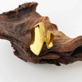 Modern sculptural bold gold statement ring displayed on natural wood with plants in the background.