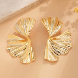 Oversized botanical gold leaf statement earrings with bold textured design displayed on a wooden surface.