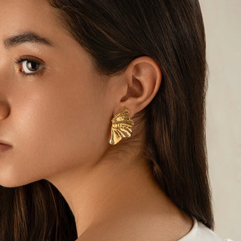 A pair of bold textured gold leaf statement earrings worn by a model, highlighting designer fashion jewelry.
