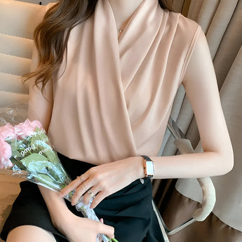 A woman wearing a vibrant green cowl neck sleeveless blouse, showcasing a stylish fashion look. The blouse features a loose drape around the neckline, with a form-fitting cut around the waist. The model's arms are exposed, emphasizing the sleeveless design of the blouse.