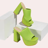 A pair of bright orange ankle boots with stretch fit sock heels featuring neon details, worn by a person standing on a floor.