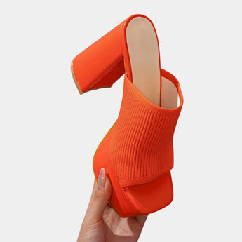 Bright orange ankle boots with stretch fit sock heels featuring neon detailing, shown being worn on a human leg.