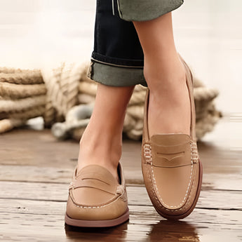 Brown leather men's slip-on loafers in size 43, featuring a stylish and comfortable design. The shoes are displayed on a wooden surface, paired with grey denim jeans, highlighting the footwear's sleek appearance.