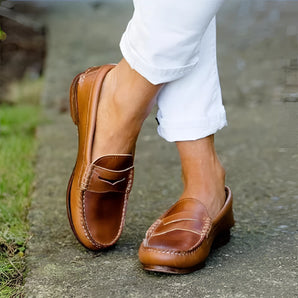 Brown leather men's slip-on loafers on a person wearing jeans, showcasing a stylish and comfortable design suitable for casual wear.