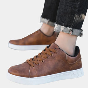 Men's brown leather low-top sneakers with a stylish design and white sole, paired with denim pants.
