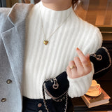 
A woman wearing a brown ribbed sweater that appears cozy and stylish for fall, paired with gold earrings. The sweater has a beige hue and features long sleeves, a high neck, and a fitted design, emphasizing the shoulders. The woman is captured with a gentle gesture, highlighting the elegance of the outfit.