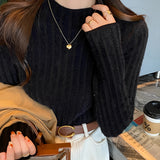 
A close-up image of a person wearing a black ribbed sweater with long sleeves, showcasing the texture and fit around the shoulders and neck. The person's hand is slightly visible, resting near the shoulder, enhancing the cozy fall chic look.