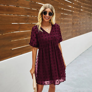 Woman wearing a burgundy floral mini dress, accessorized with sunglasses, smiling outdoors.
